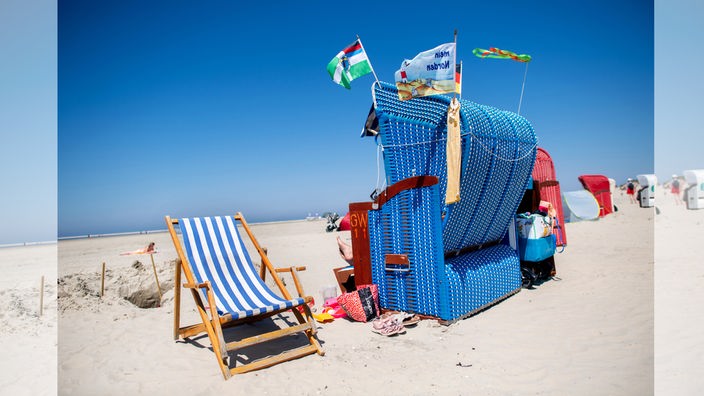 Ein mit verschiedenen Flaggen geschmückter Strandkorb steht bei sonnigem Wetter am Strand der Insel Borkum.