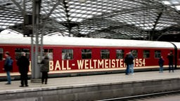 Ein roter Zug mit der Aufschrift "Fußball Weltmeister 1954" an einem Gleis in einer Bahnhoshalle.
