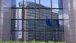 Das Berlaymont-Gebäude und eine EU-Flagge spiegeln sich in eienr Glasfassade. 