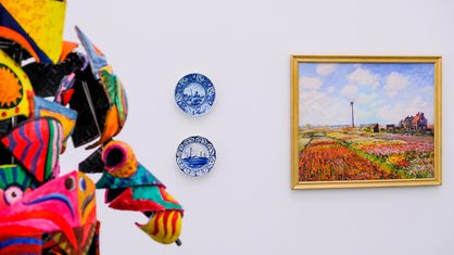 Ausstellungsansicht "Die Grosse" im Museum Kunstpalast in Düsseldorf: Ein Gemälde neben Wandtellern, im Vordergrund eine bunte Skulptur.