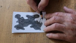 Filmstill "Rückriem zeichnet" von Lucas Rückriem: Nahaufnahme vom Entstehungsprozess einer kleinen Stift-Zeichnung mit amorpher Form.