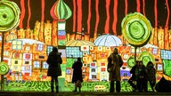 Besucher sehen digital beleuchtete Multimedia-Kunstwerke des österreichischen Künstlers Friedensreich Hundertwasser im Phoenix des Lumières in Dortmund.