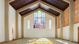 Ein großer leerer ehemaliger Kirchenraum, mittlerweile mit japanischer Anmutung, durch dessen bunte Glasfenster hellen Licht einfällt.