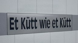 An einem Wohnhaus in Köln steht eine kölsche Redewendung "Et Kütt wie et Kütt".