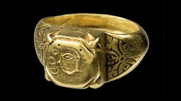 Ein goldner Ring mit Verzierungen vor schwarzem Hintergrund.