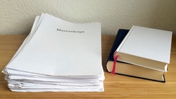 Symbolbild: Ein Stapel Papier mit der Aufschrift "Manuskript, daneben zwei gebundene Bücher.