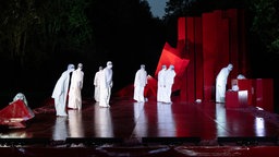 Szenefoto von "Ödipus" am Theater an der Ruhr in Mülheim: Mehrere ganz in weiß gehüllte Menschen auf einer Freilichtbühne blicken in dieselbe Richtung.