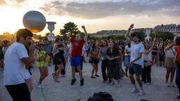 Symbolbild: Menschen tanzen im Tuileriengarten vor einem Musiker mit Mikrofon, im Hintergrund die Mongolfiere mit dem olympischen Feuer.