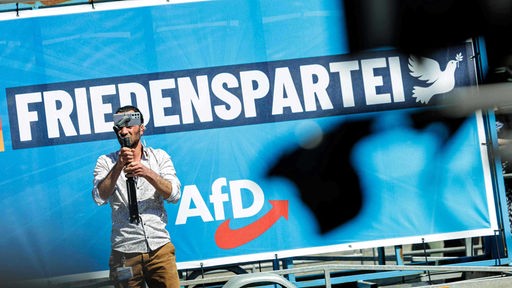 Ein Mann filmt sich vor einem Plakat mit der Aufschrift "Friedenspartei AfD"