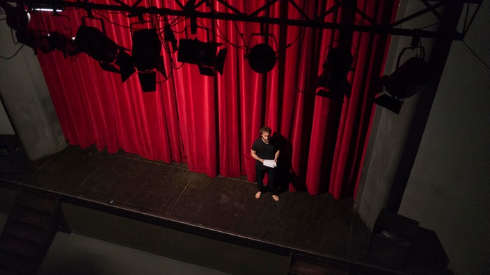 Schauspieler mit Skript auf einer Bühne mit rotem  Vorhang