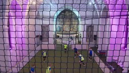 Einge Personen spielen in der Kirche von Wettringen Soccer auf einem von einem Netzt abgeschirmten Feld.