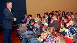 Kinder sitzen mit Erziehungsberechtigen im Publikum eines Puppentheaters.