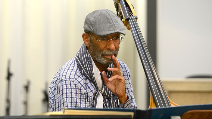 Der Jazzbassist Ron Carter betrachtet, neben seinem Instrument sitzend, ein Notenbuch.