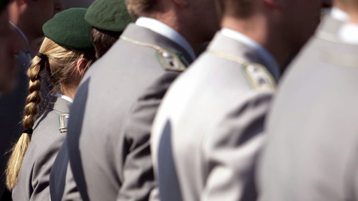 Bundeswehrsoldatin mit langem, blonden Zopf steht inmitten ihrer männlichen Kameraden