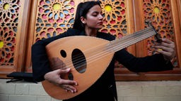 Eine junge iranische Musikerin mit dunklen Haaren, hält eine Oud in der Hand und stimmt sie.