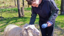 Tonart-Reporter Jan Klefisch steht auf der Schafweide mit einem Schaf.