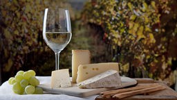 Weinglas und Käse angerichtet auf einem Tisch in Weinbergen.