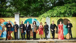 Das Ensemble "La Venexiana" steht mit Instrumenten vor einer bunten Wand