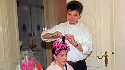 Ein Friseur dreht die Haare einer Kundin für eine Dauerwelle auf spezielle Papilloten.