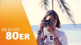 Ein Mädchen knipst mit einer analogen Kamera am Strand