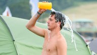 Ein Festivalbesucher schüttet sich wegen der Hitze auf dem Campingplatz Wasser über den Kopf