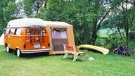 Ein VW Bus steht mit einem Vorzelt auf einem Campingplatz. (1985) 