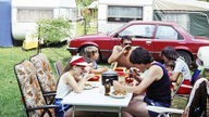Eine Familie isst gemeinsam auf dem Campingplatz (1970er)