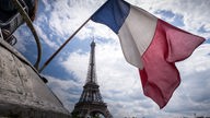 Eine französische Flagge vor dem Eiffelturm in Paris