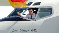 John Travolta hält die deutsche Flagge aus dem Cockpit seines Flugzeuges bei seiner Landung in Frankfurt 2002.