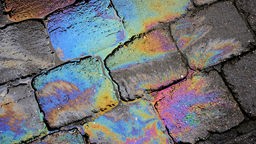 Ein Ölfleck auf einem Kopfsteinpflaster in Dudweiler schimmert in Regenbogenfarben