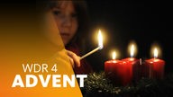 Ein Kind zündet Kerzen eines Adventskranzes an