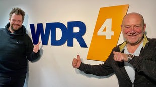 Paveier (Sven Welter, l., und Detlef Vorholt, r.) vor WDR 4 Logowand