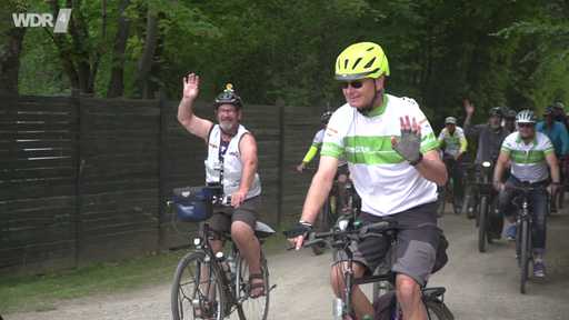 Zwei Radfahrer bei der NRW Radtour lächeln in die Kamera und winken fröhlich