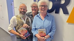 Die Buchclub-Mitglieder Dirk Klauke, Ruth Lobach und Susanne Ludwig stehen vor dem WDR 4-Logo