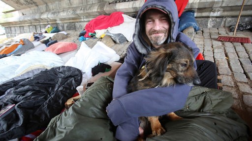 Der obdachlose Slowake Stano lächelt, während er bei Temperaturen um den Gefrierpunkt mit seinem Hund Mob im Arm zwischen Decken und Matratzen unter einer Brücke