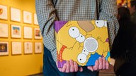 Ein Mann hält hinter seinem Rücken ein Buch über die Simpsons in der Ausstellung "Die Simpsons: Gelber wird's nicht" in Dortmund.