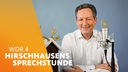 Dr. Eckart von Hirschhausen sitzt neben einem Vogelhaus und vor einem Mikrofon