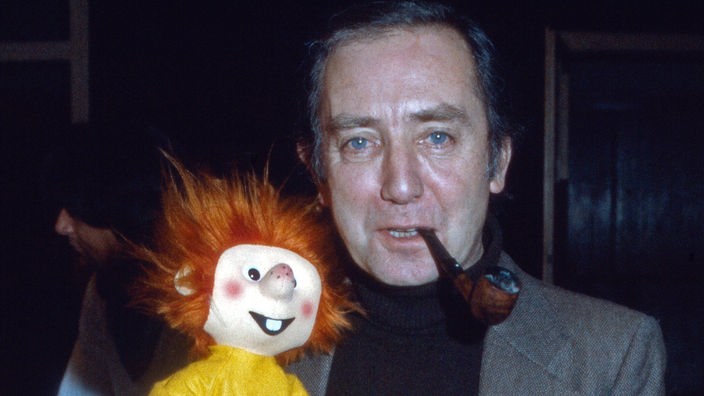 Synchronsprecher Hans Clarin mit Pfeife im Mund und Pumuckl-Puppe auf dem Arm (1983)