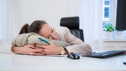 Eine junge Frau schläft in einem Büro am Schreibtisch