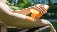 Eine Frau cremt im Park ihre Unterarme mit Sonnencreme ein