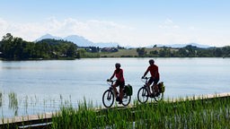 Paar mit E-Bikes fährt am Uferweg eines Sees