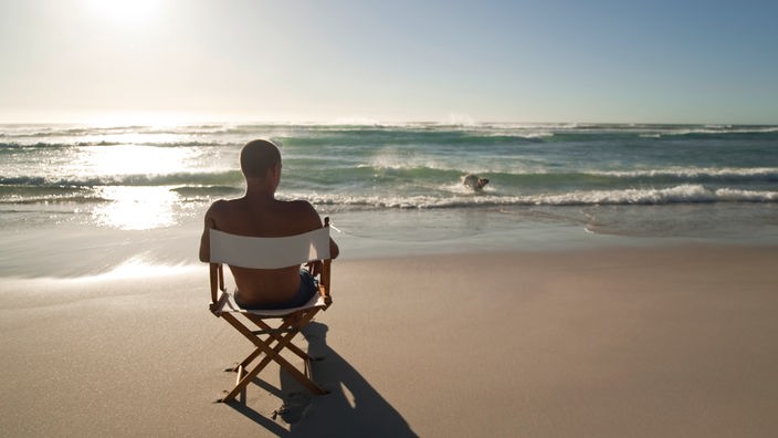 Ein Mann sitzt in einem Klappstuhl am Strand und liest