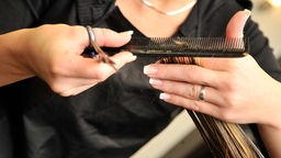 Frau schneidet Haarsträhne mit Schere und Kamm