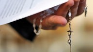 Ein Priester hält einen Rosenkranz und eine bischöfliche Erklärung zu den Missbrauchsfällen durch Jesuiten-Pater in der Hand. 