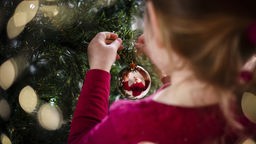 Ein Mädchen schmückt den Weihnachtsbaum