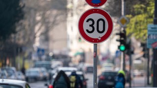 Auto- und Radfahrer passieren ein Verkehrschild in einer Zone mit 30 Kilometern Geschwindigkeitsbeschränkung
