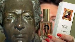 Zwischen der Bronzebüste Heinrich Heines und der Schachtel des Parfüms hält eine Museumsmitarbeiterin die Parfümflasche in die Kamera.