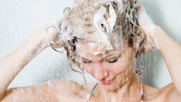 Frau wäscht sich unter der Dusche die Haare mit Shampoo.