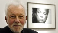 Der Fotograf Robert Lebeck posiert in seiner Ausstellung, im Hintergrund ein Portraet von Willy Brandt, in der Galerie 