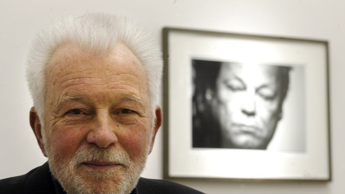 Der Fotograf Robert Lebeck posiert in seiner Ausstellung, im Hintergrund ein Portraet von Willy Brandt, in der Galerie 
